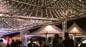 Large clear-span event tent with string lighting for an outdoor wedding or evening celebration.