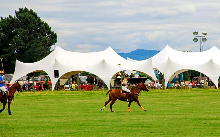 White tensile fabric event tents on a grassy field during an outdoor equestrian event.