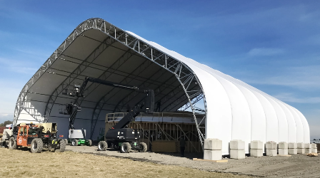 Large fabric-covered construction tent sheltering heavy equipment and materials on an active construction site